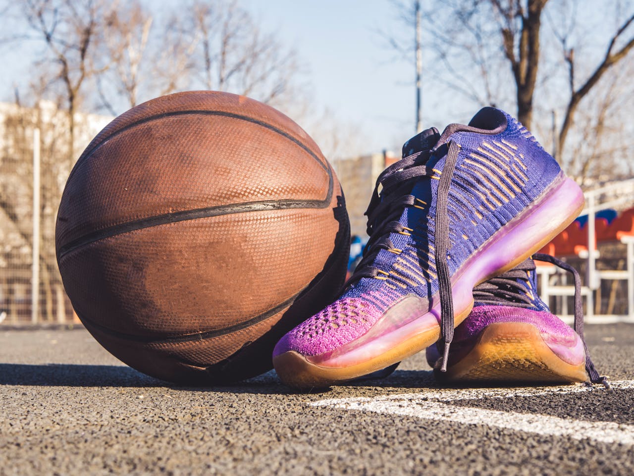Close-up of sneakers and a basketball on an outdoor court, emphasizing sports and urban style.
