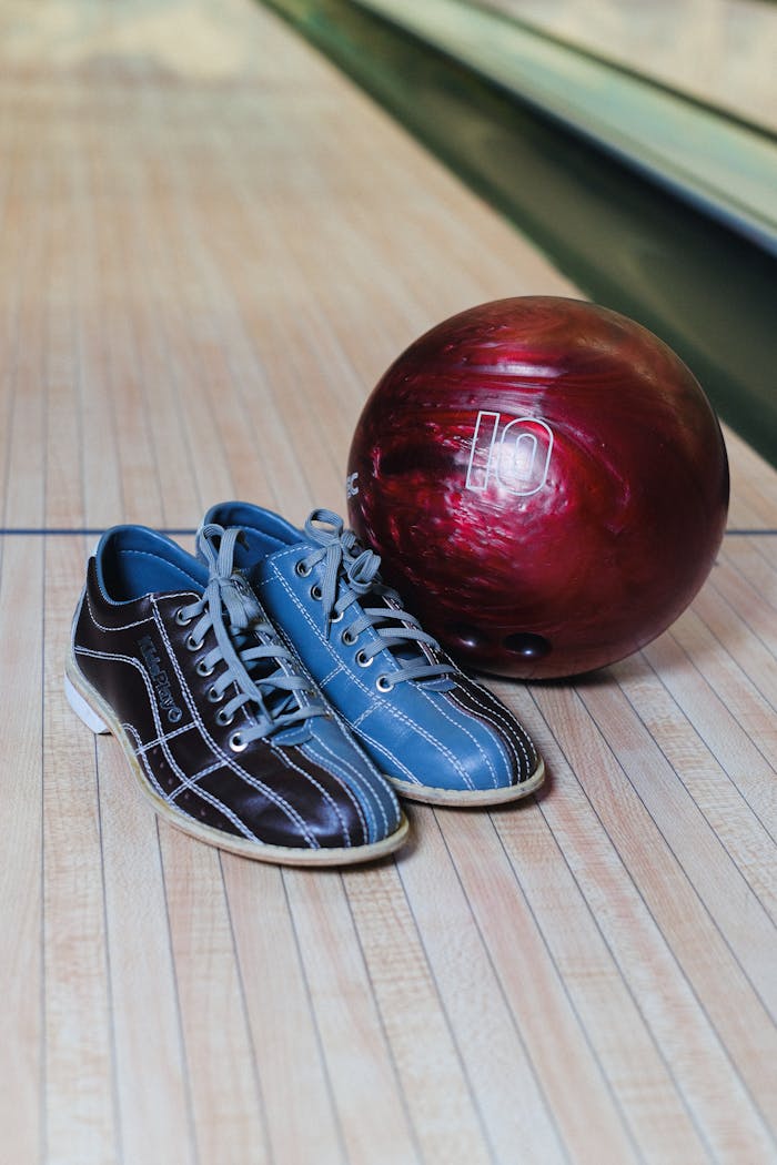 A pair of colorful bowling shoes beside a maroon bowling ball on a wooden lane.